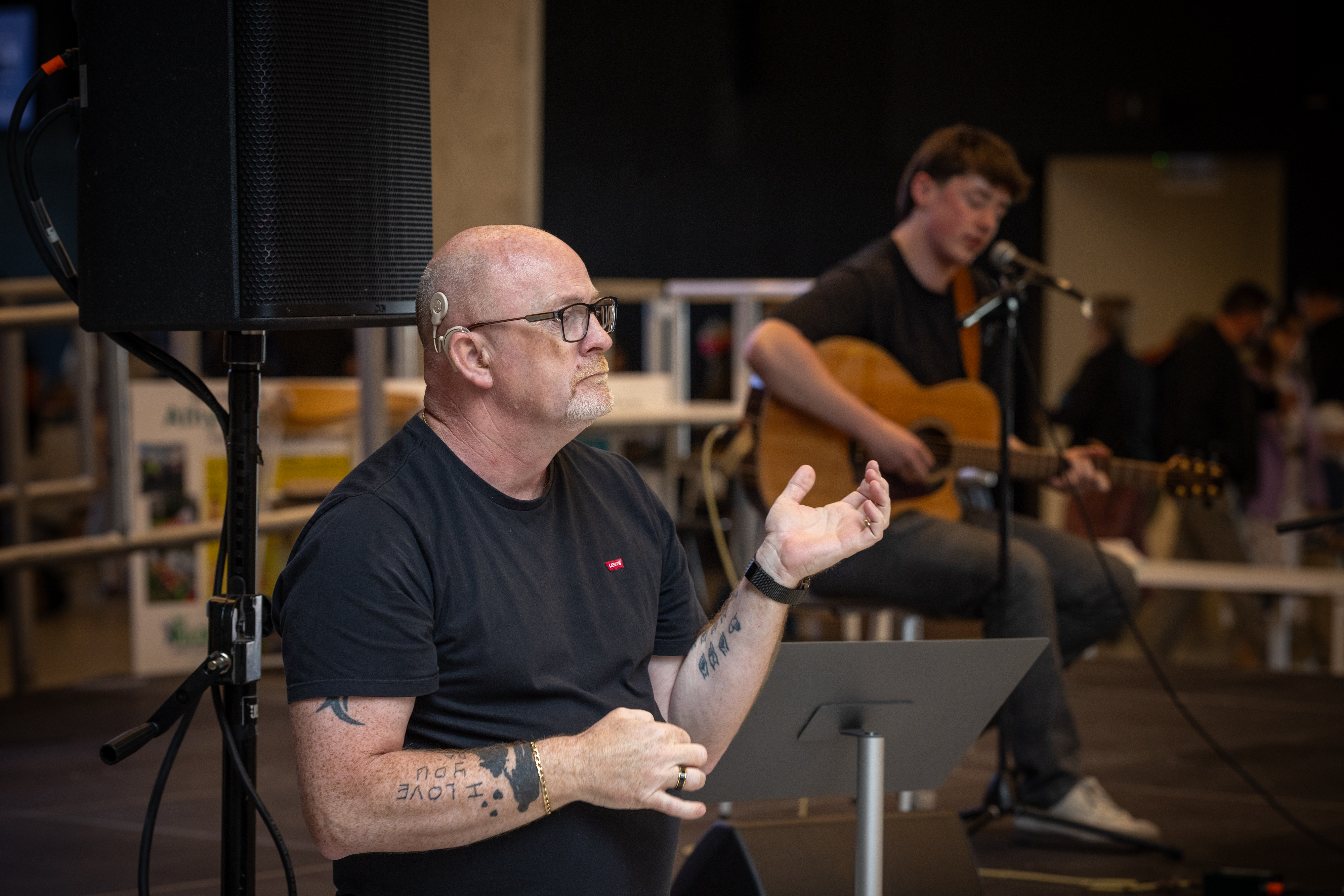 A person singing on stage with playing guitar , accompanied by a sign language interpreter. 